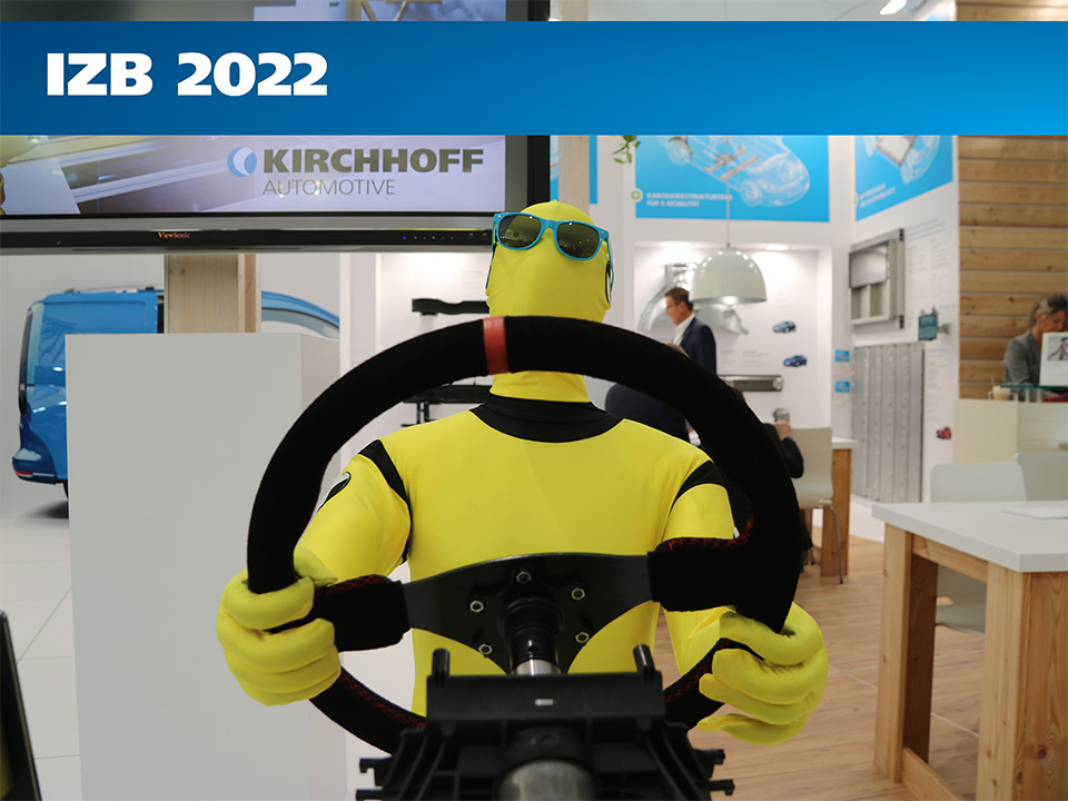 Eine Person in einem gelben Ganzkörperanzug und einer blauen Sonnenbrille hält an einem Messestand von Kirchhoff Automotive ein Lenkrad in der Hand.